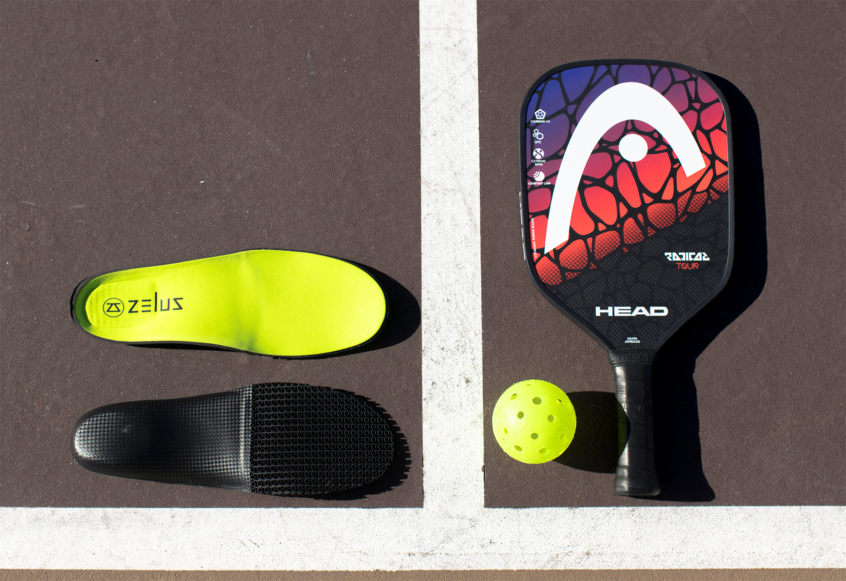 Zelus insoles laying on a pickleball court next to paddle and ball